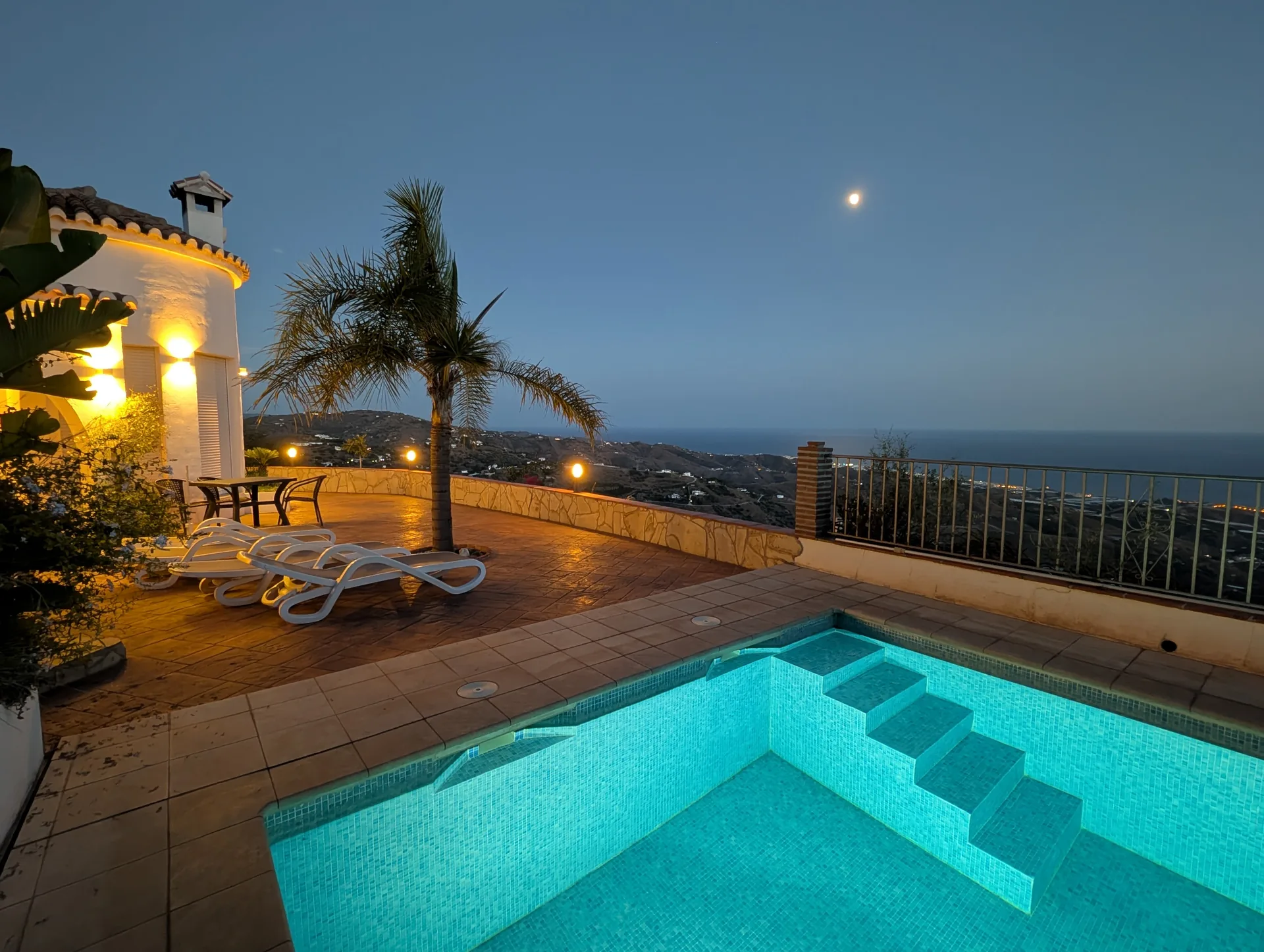 Beleuchteter privater Pool mit Terrasse und Meerblick am Abend